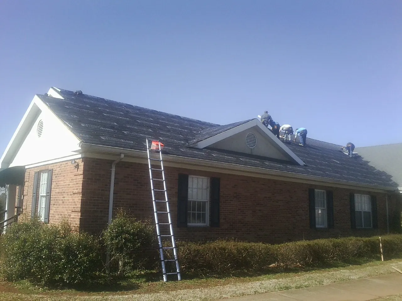 Crew tearing shingles off a brick ranch roof with a ladder set — Metal Roof Repair work by our crew in Ansted