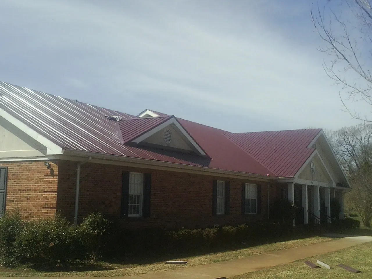 Red metal roof with gabled entries on a long brick building, from a Hail Damage Roof Repair job in Ansted