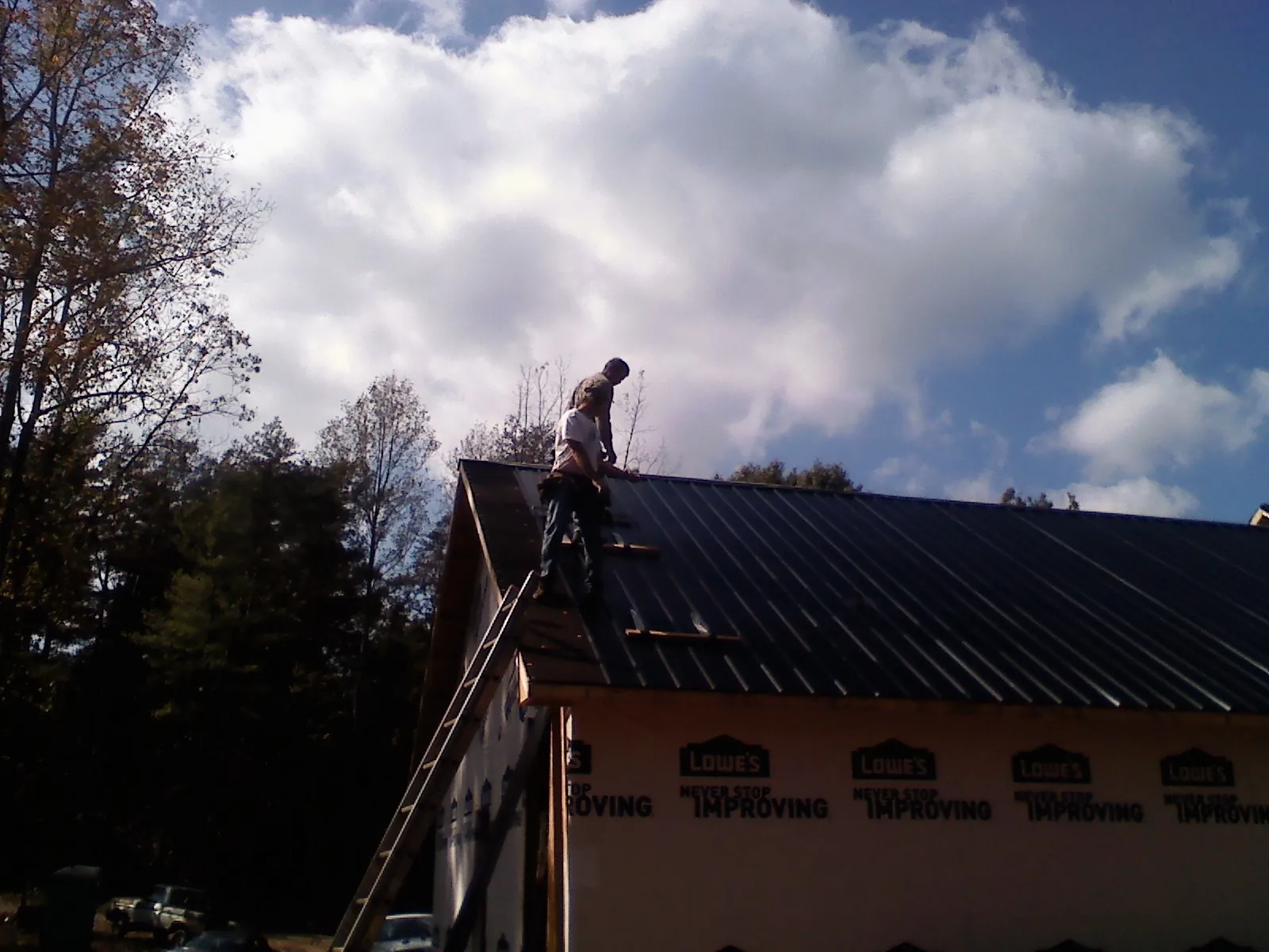 Roofer fastening dark metal panels high against a cloudy sky, from a Roof Inspection job in Ansted