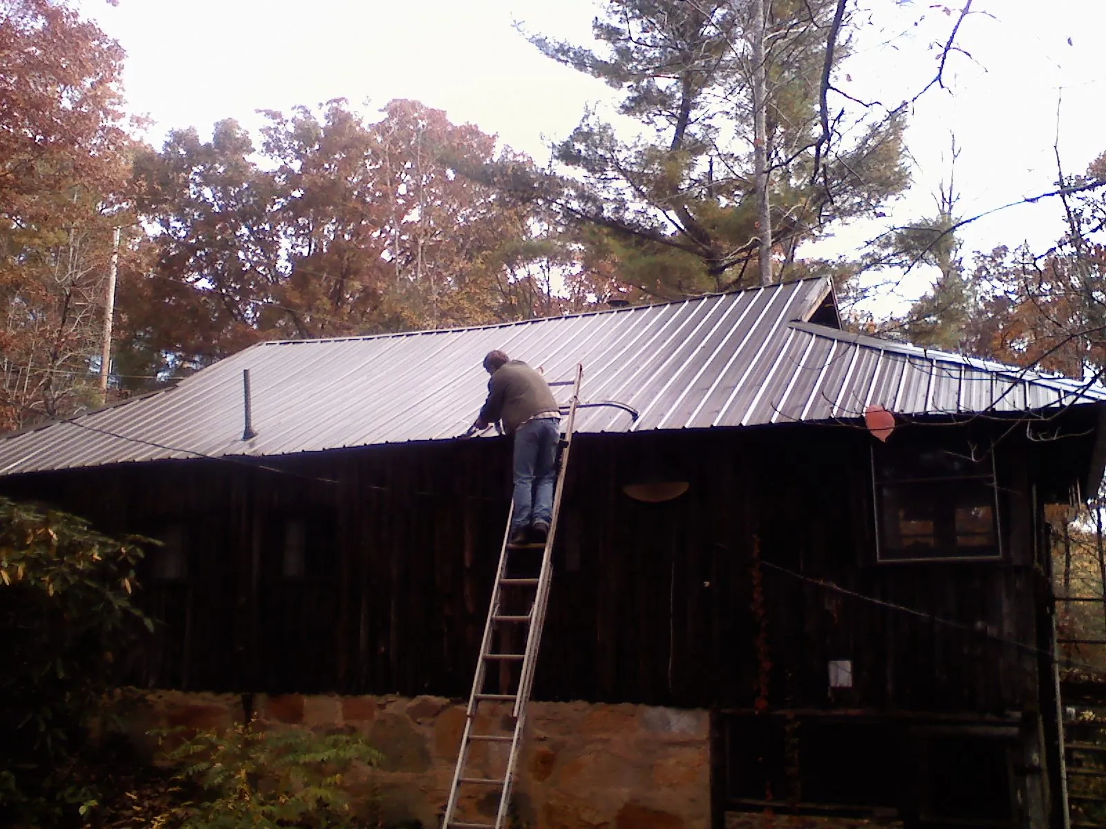 Roofer on a ladder working along the edge of a cabin metal roof in Ansted