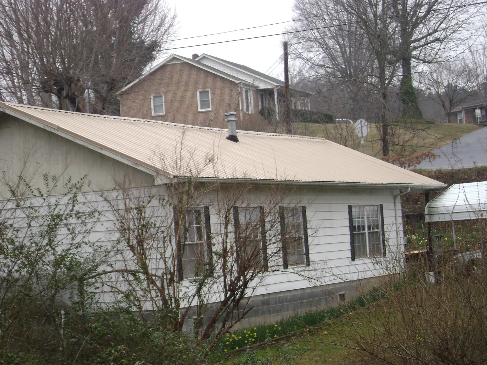 Tan metal roof on a white sided house set into a hillside — Commercial Roofing by Roofing Brothers in Ansted