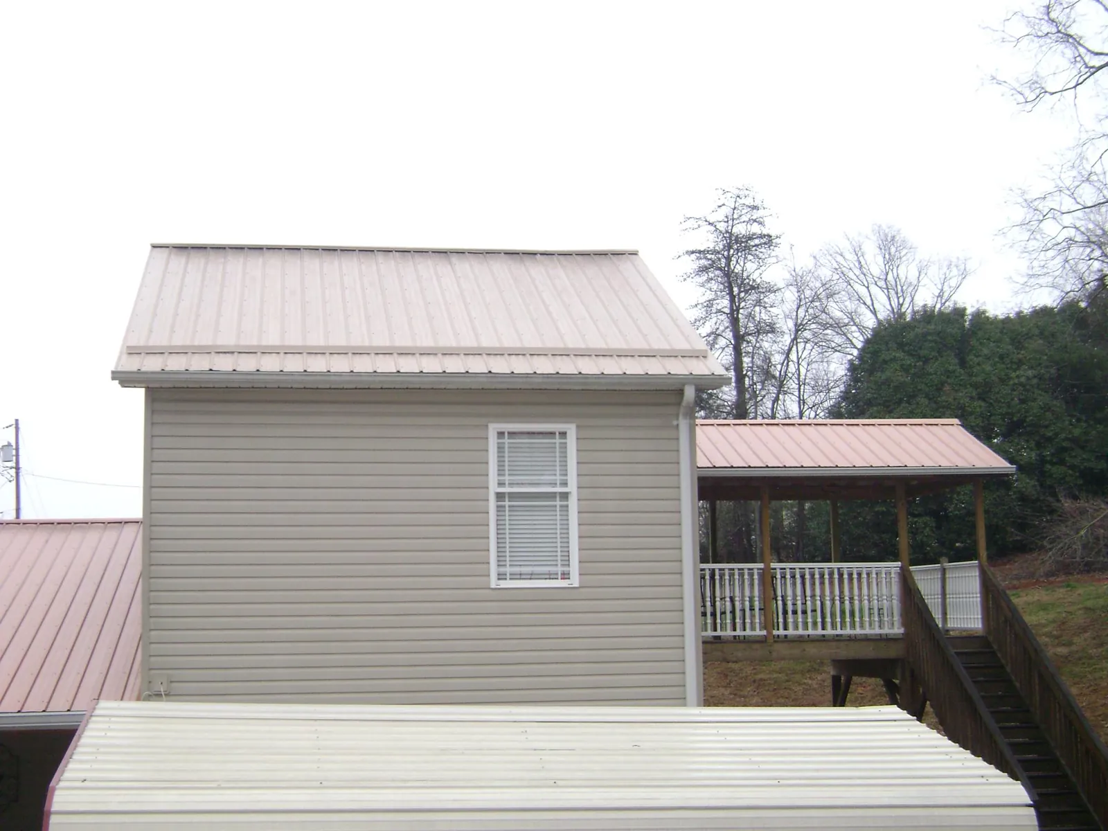 Tan metal roofs on a two story addition and attached porch, from a Roof Replacement job in Ansted